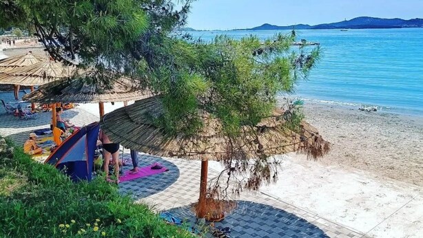 Una spiaggia con una struttura a tetto di paglia, una tenda e una persona su un tappetino da yoga.