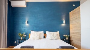 Uma cama de casal com cabeceira de madeira, duas mesas de cabeceira com plantas e uma parede azul de destaque.