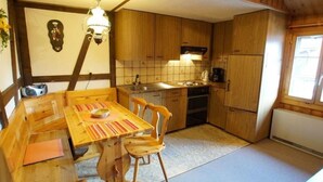 A compact kitchen with wooden cabinets, a dining table with chairs, a built-in oven, and a window providing natural light. - Fontauna Degonda by Interhome (Sedrun)