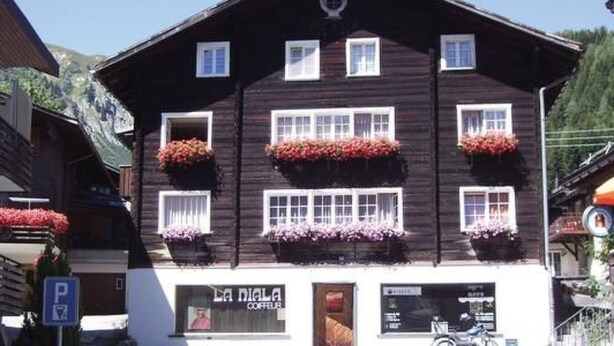 A two-story building with a dark wooden facade, multiple windows with white frames, and flower boxes on the second floor. - Fontauna Degonda by Interhome (Sedrun)