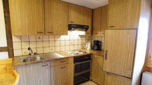 A compact kitchen with wooden cabinets, a built-in oven, a coffee maker, and a refrigerator. - Fontauna Degonda by Interhome (Sedrun)
