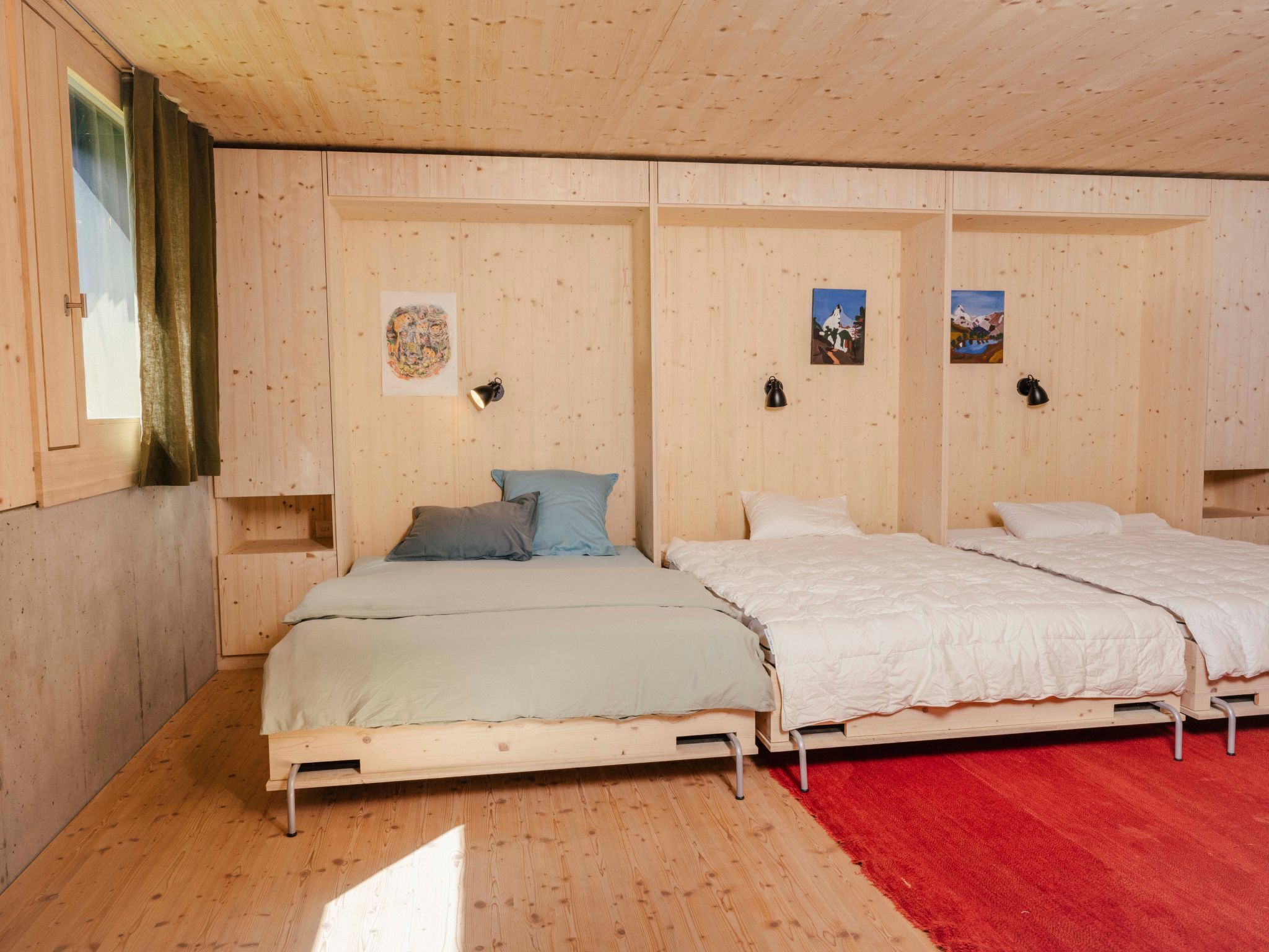 A wooden room with two beds, a red carpet, and wall-mounted lamps.