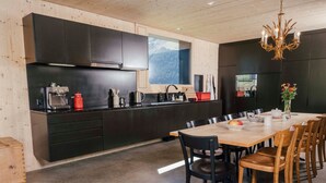 Une cuisine moderne avec des meubles de couleur sombre, une table à manger en bois et un lustre.