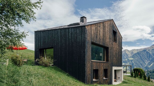 Une maison moderne avec un toit en pente, de grandes fenêtres et un petit espace porche.