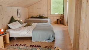 Une chambre confortable, aménagée dans un chalet en bois, avec deux lits, une chaise et une grande fenêtre.
