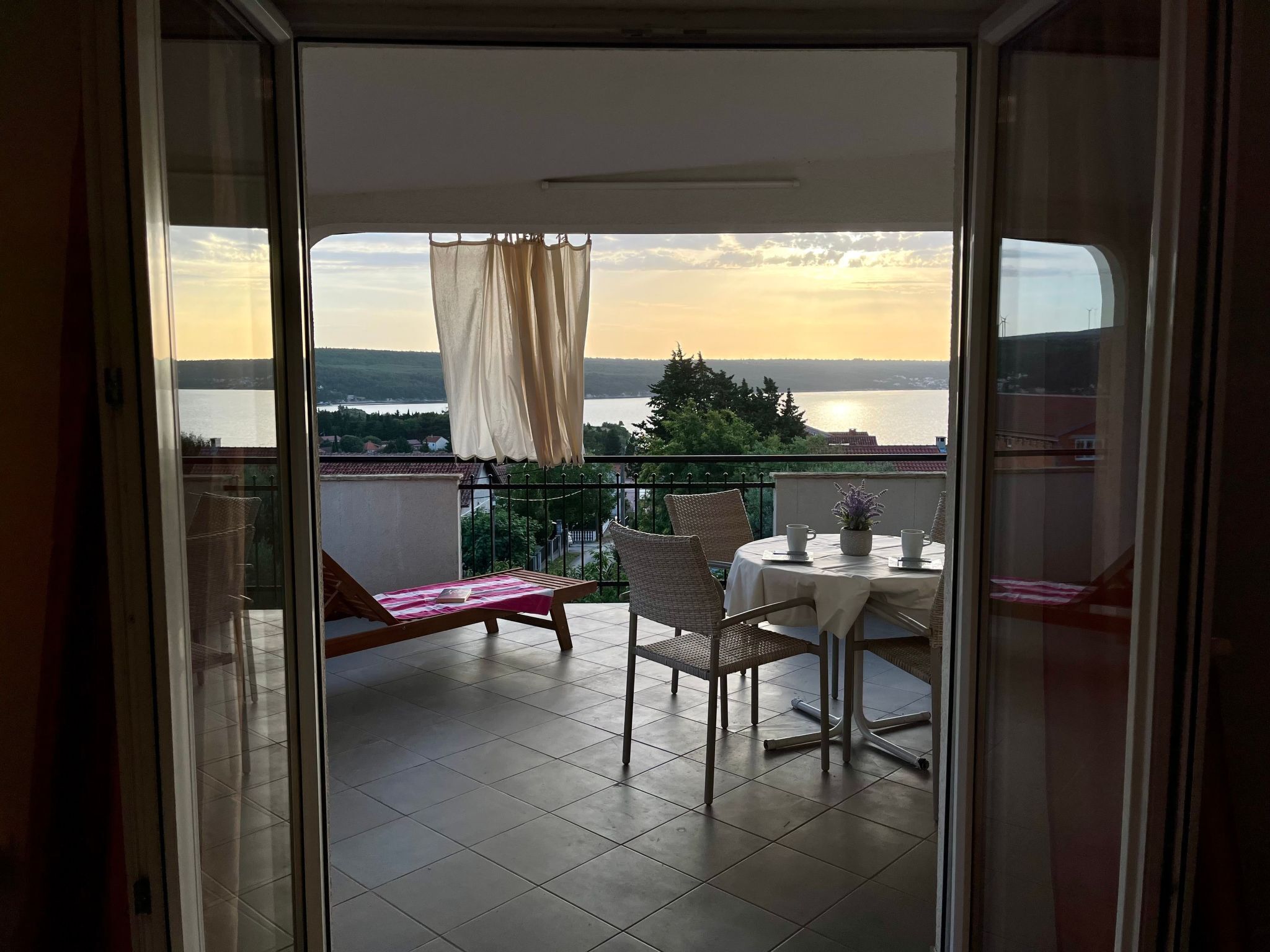 Un balcon avec une table et des chaises, une vue sur un lac et un coucher de soleil.