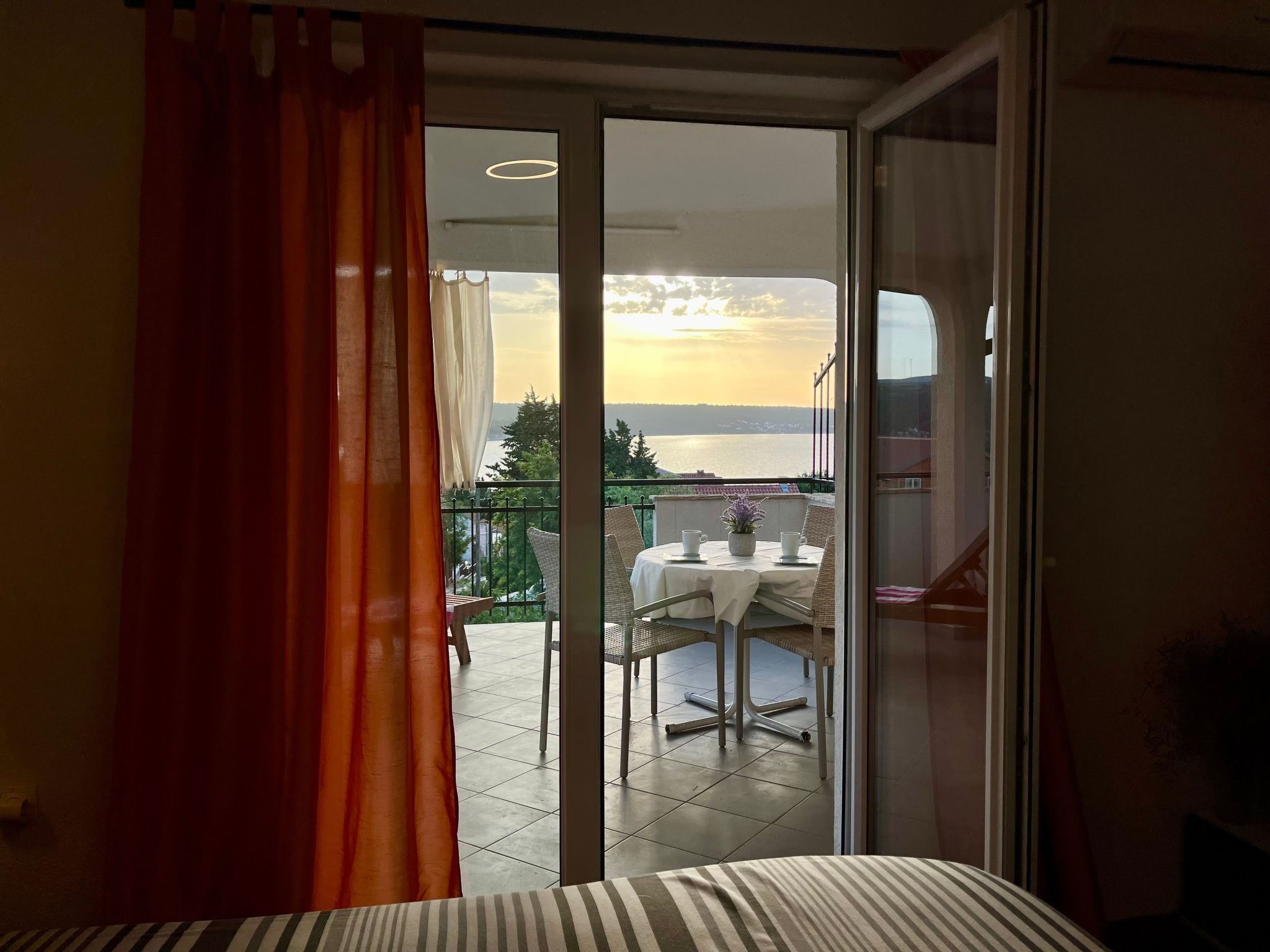 Ein Balkon mit Tisch und Stühlen, Blick auf das Meer und ein Sonnenuntergang.