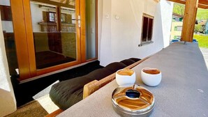 Un área de estar exterior moderna con una mesa de piedra, dos tazas de cerámica blanca y un banco de madera.