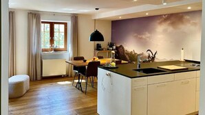 Una cocina moderna con una isla central, un comedor con mesa y sillas, y un amplio ventanal con cortinas.