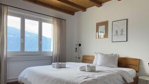 A bedroom with a large bed, wooden headboard, white bedding, a window with curtains, and two framed pictures on the wall. - Casa Campanula by Interhome (Laax)