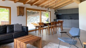 A modern interior with a wooden ceiling, a dining area, a kitchen, and a living room with a sofa and coffee table. - Casa Campanula by Interhome (Laax)