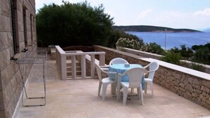 Una terrazza esterna con un muro in pietra, un tavolo e sedie, e vista sul mare.