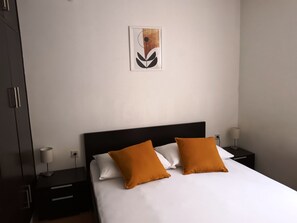 A neatly made bed with white and orange pillows, a black headboard, and a framed artwork on the wall. - "Appartement "Ana"" by Interhome (Brač/Povlja)