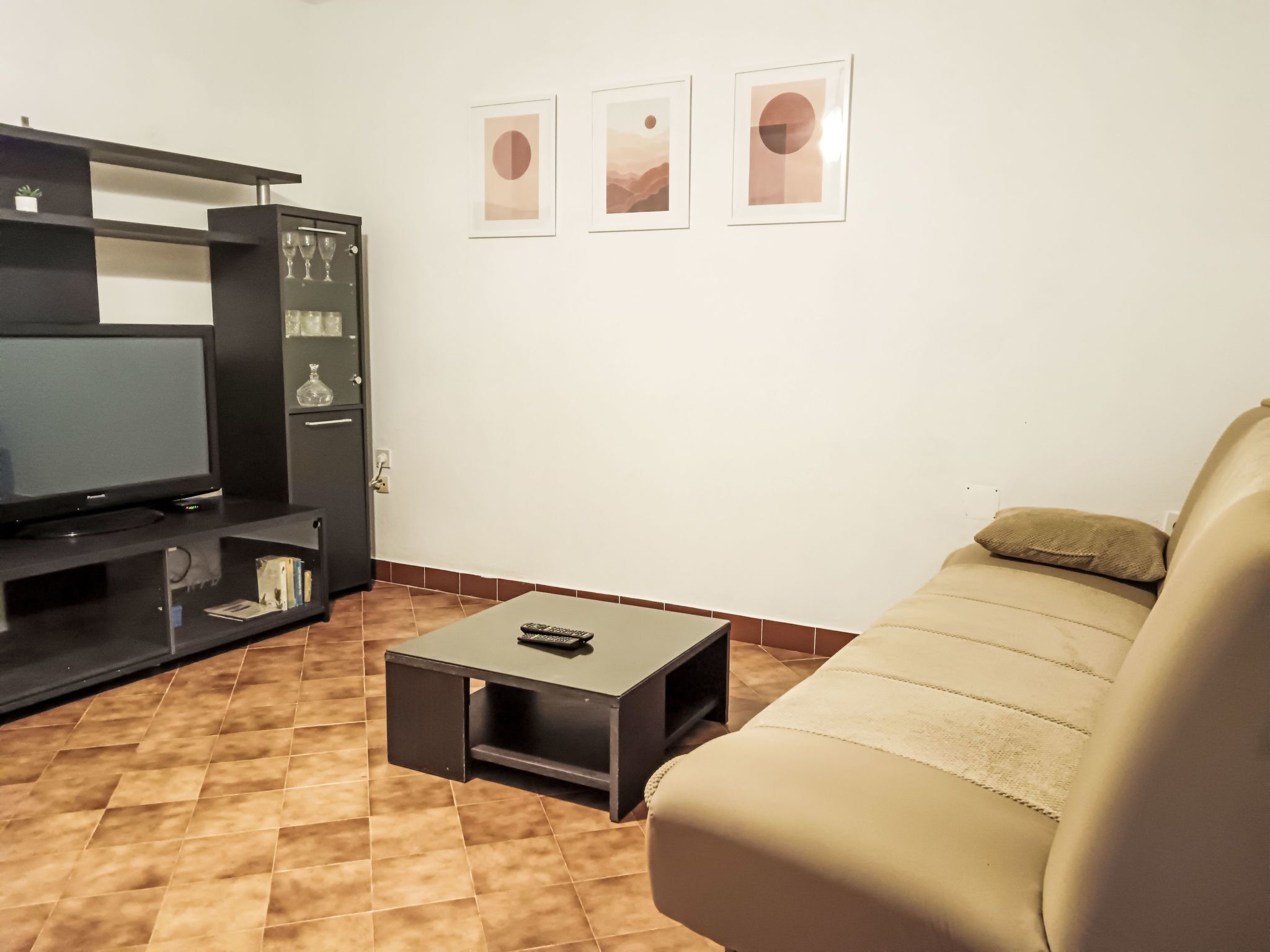 Ein Wohnzimmer mit Fernseher, einer Couch, einem Couchtisch und einer Vitrine mit Weingläsern.