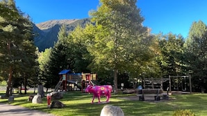 En park med en lekplats, en rosa koskulptur och ett berg i bakgrunden.