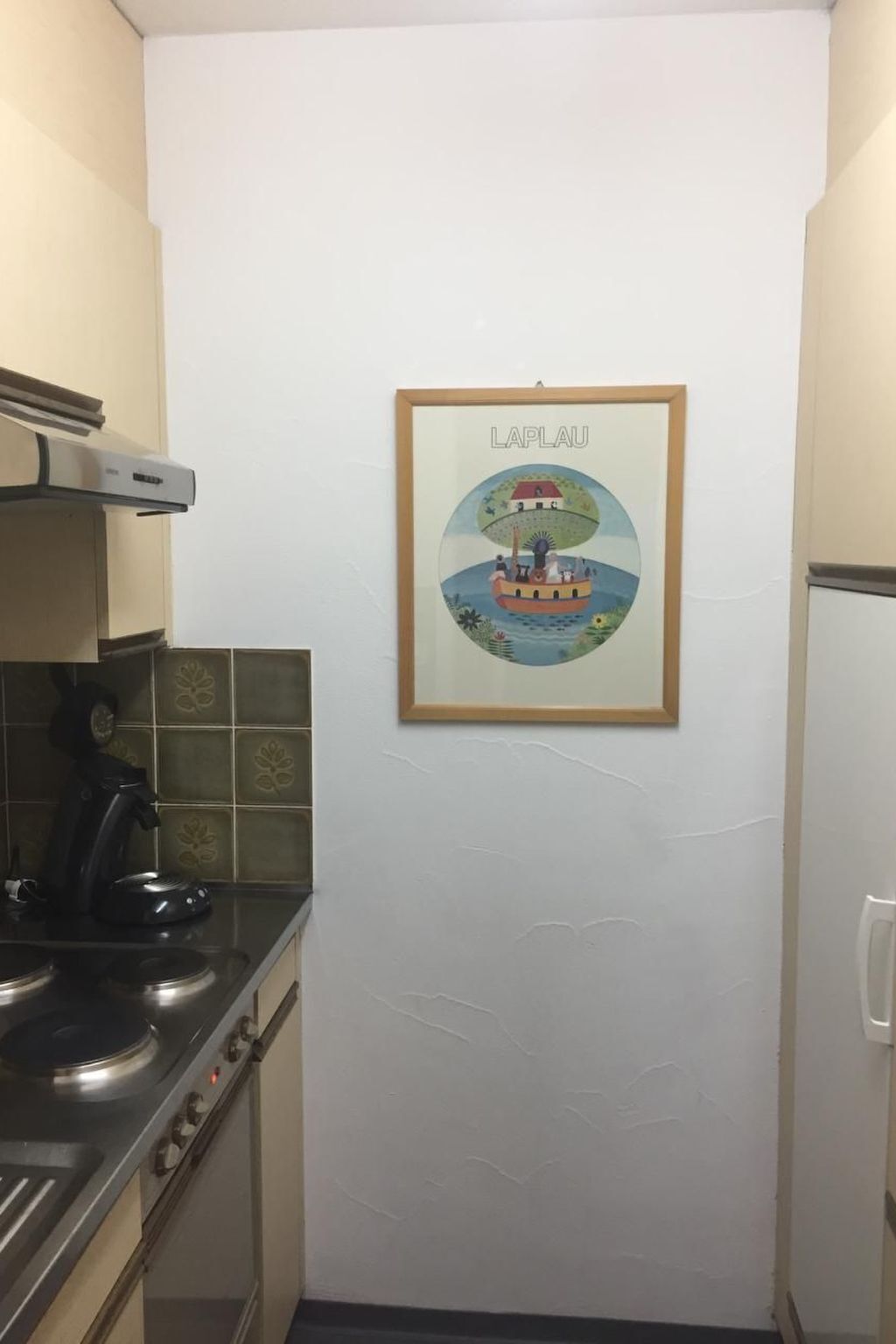 A kitchen with a stove, a kettle, and a framed picture on the wall.
