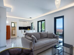 Ein modernes Wohnzimmer mit grauem Sofa, Essbereich und Küche.
