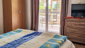 A bedroom with a bed, a wooden wardrobe, a television, and a sliding glass door leading to an outdoor patio. - Apartment am See by Interhome (Balatonmariafurdo)