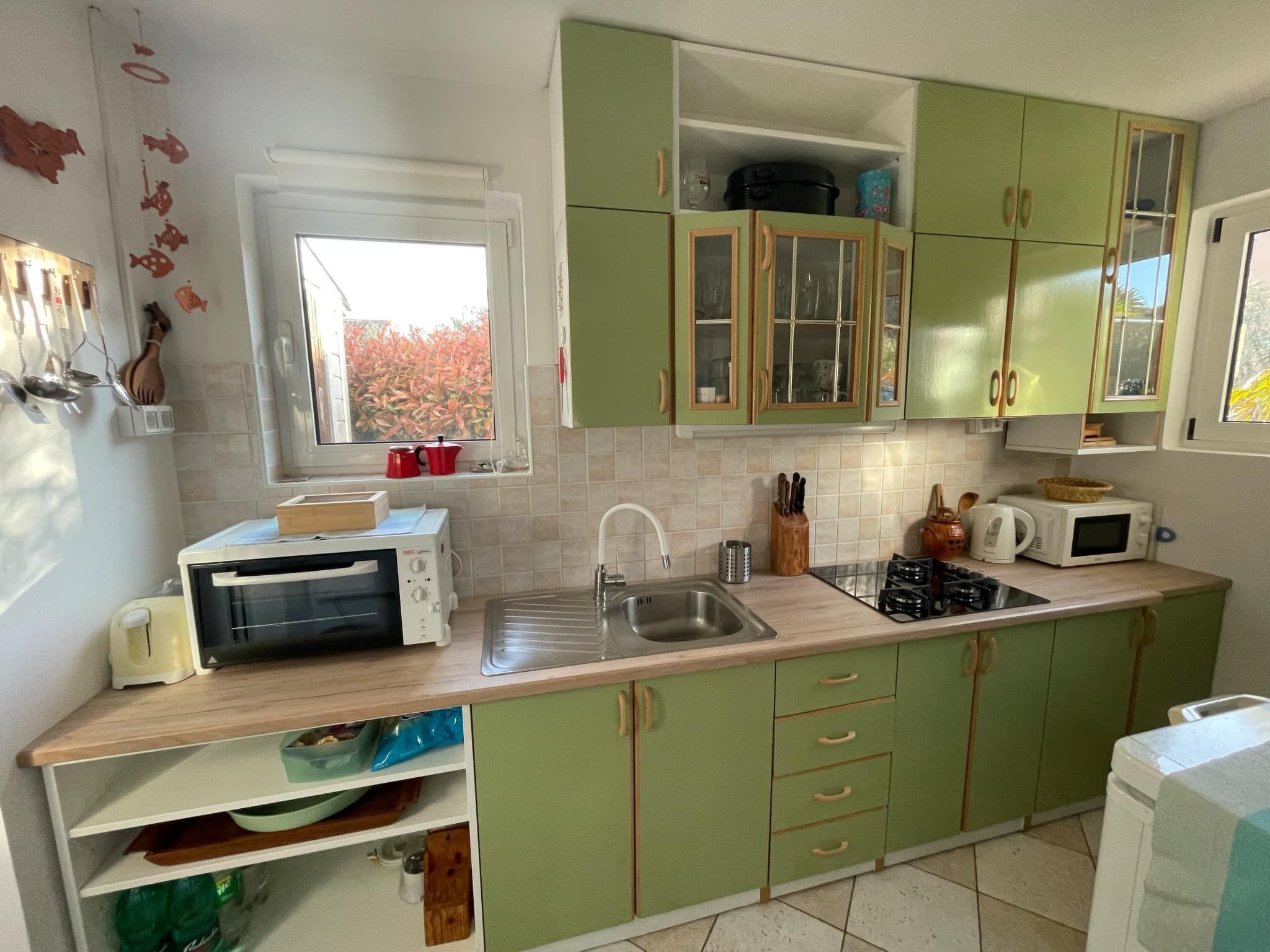 Una cocina con gabinetes verdes, una ventana, un fregadero, una estufa y un microondas.