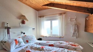 A bedroom with two beds, a window with curtains, a lamp, and a wooden ceiling. - Sin Sponda by Interhome (Vaz)