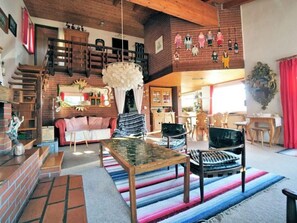 Uma sala de estar ampla com escada de madeira, mesa de centro de vidro e tapete listrado e colorido.