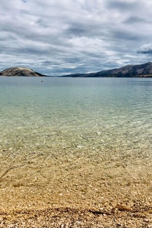 Un lago cristalino con una orilla rocosa y montañas a lo lejos.