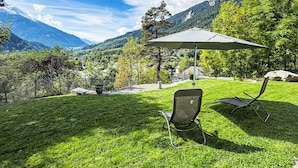 A grassy outdoor area with a chair and umbrella, overlooking a mountainous landscape.