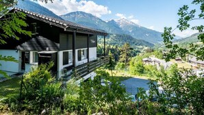 A modern chalet with a balcony overlooking a valley and mountains.