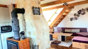 A cozy loft-style living space with a stone wall, a wood-burning stove, a wooden dining table, and a comfortable seating area. - Haus Laura, Radslav by Interhome (Cerna v Posumavi)