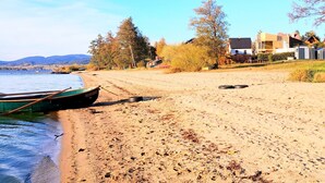 A beach with a rowboat, sandy shore, trees, and buildings in the background. - Haus Laura, Radslav by Interhome (Cerna v Posumavi)