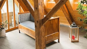 A cozy attic room with a wooden beam ceiling, a cushioned bench, and a small table with a lantern.
