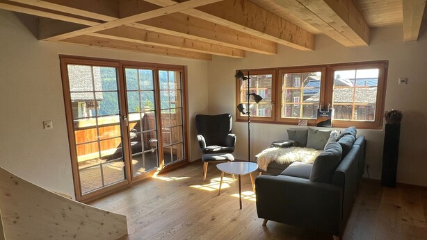 A spacious living room with wooden floors, a sofa, a chair, and a small table. Large sliding glass doors lead to an outdoor area. - Steirufina by Interhome (Bellwald)