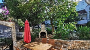 Eine Außenpatio mit einem Steintisch, Holzstühlen, einem roten Sonnenschirm und einer Steinmauer.