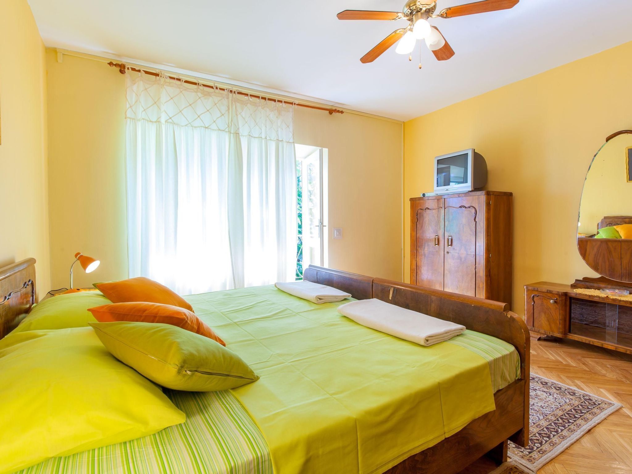 Een slaapkamer met een bed, een houten garderobe, een bureau met spiegel en een plafondventilator.