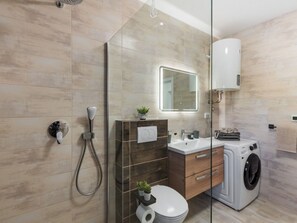 A modern bathroom with a glass shower enclosure, a built-in toilet, a washing machine, and a vanity with a mirror. - Vacation home  by Interhome (Vir)