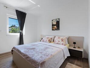 A bedroom with a bed, a nightstand, a lamp, a window with curtains, and a painting on the wall. - Vacation home  by Interhome (Vir)