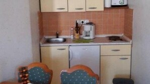 Cocina compacta con un lavamanos, una cafetera y un cubo de basura. Hay una mesa de comedor con sillas.