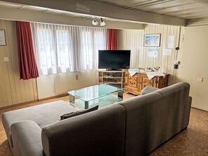 Un salon comprenant un canapé, une table basse en verre, un meuble en bois, un téléviseur et des rideaux.