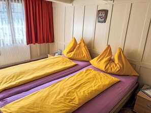 Une chambre avec deux lits, chacun agrémenté d’oreillers jaunes et de draps violets.