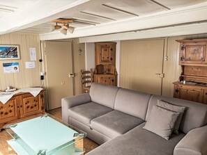 A living room with a grey sofa, wooden cabinets, a glass coffee table, and a ceiling fan. - Wenger 5-Bettwohnung by Interhome (Meiringen)