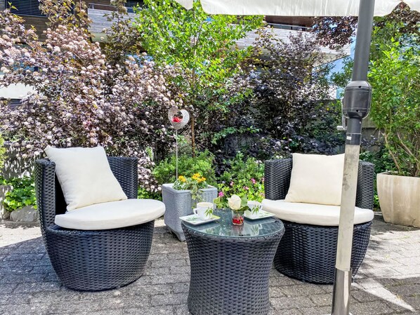 Two wicker chairs with white cushions, a small table with a glass top, and a decorative flower arrangement. - Wenger 5-Bettwohnung by Interhome (Meiringen)