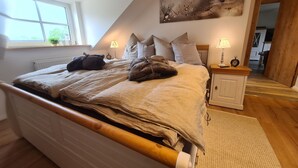 Un dormitorio con techo inclinado, una cama con cabecera de madera, dos mesitas de noche con lámparas, un radiador y un cuadro en la pared.