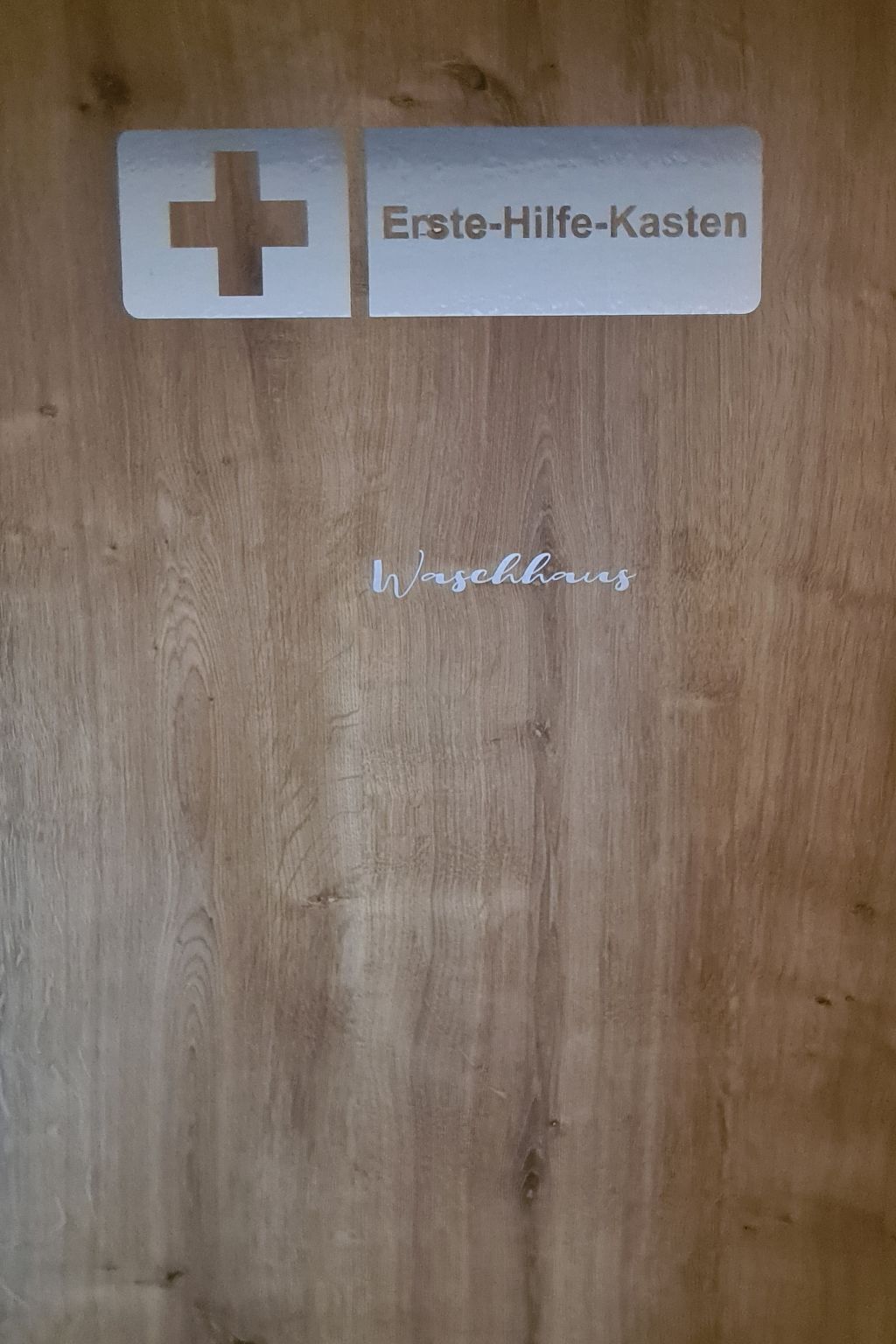 A wooden door with a white sign that reads "Erste-Hilfe-Kasten" and "Waschküche".