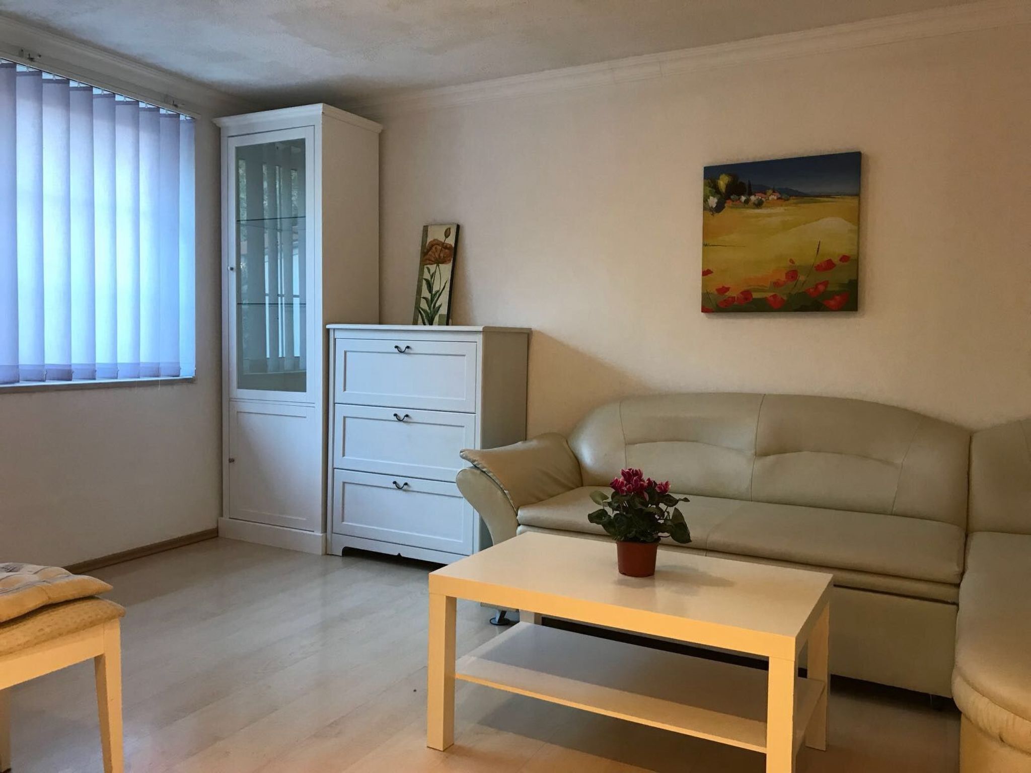 Un salon avec un canapé beige, une petite table, un meuble et un tableau accroché au mur.