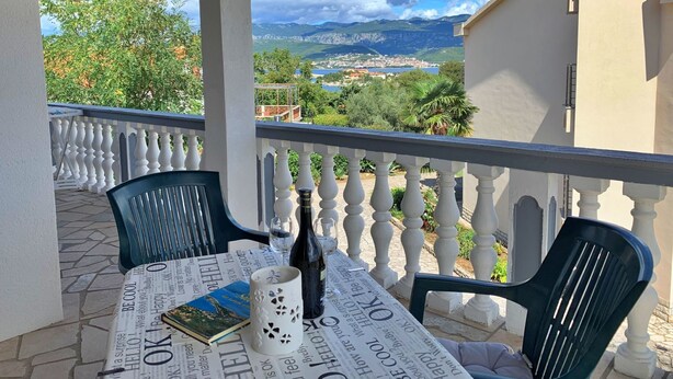 Een balkon met een tafel voor twee, met een boek, een fles en een decoratieve mok.