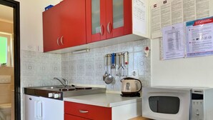Een kleine keuken met rode kastjes, een spoelbak, waterkoker en magnetron.