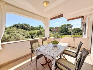 Ein Balkon mit Tisch und Stühlen, einem Blumentopf und Blick auf Grünflächen und Gebäude.