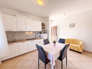 A compact kitchen with white cabinets, a tiled backsplash, a microwave, and a dining area with a table and chairs. - Apartment Nevenka by Interhome (Polje)