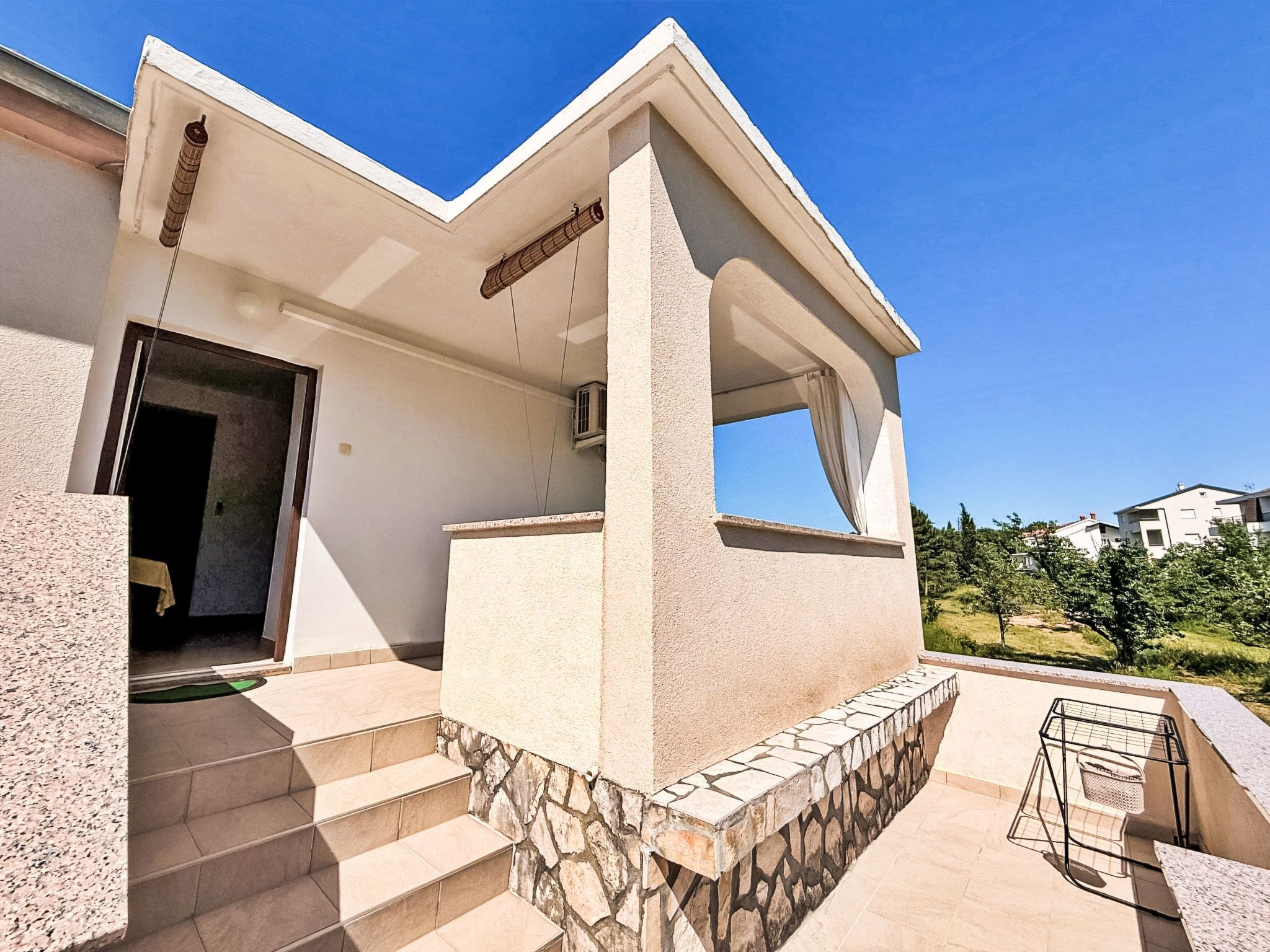 A modern building with a stone base, a flat roof, and a covered outdoor area with steps leading to a door.