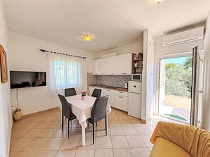 A compact kitchen with a dining area, a TV mounted on the wall, and a view through the open door. - Apartment Nevenka by Interhome (Polje)